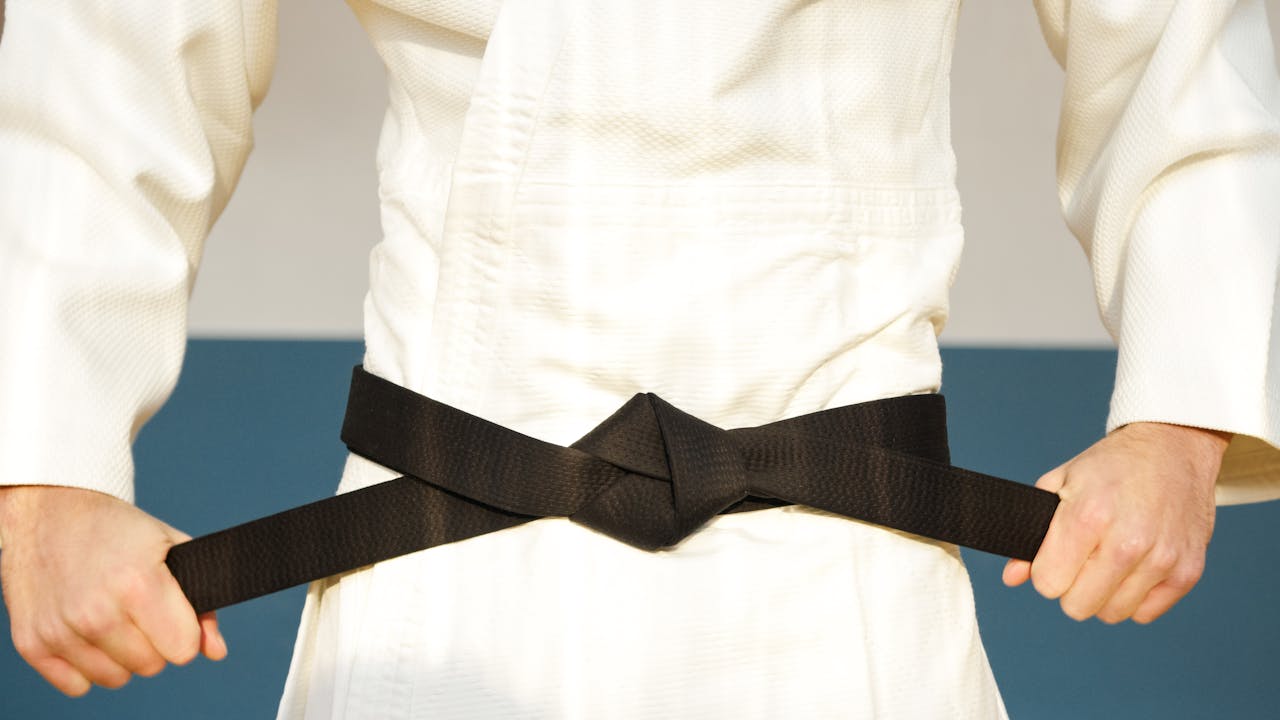 why-choose-us Detailed close-up of a martial artist adjusting a black belt on white karategi uniform.