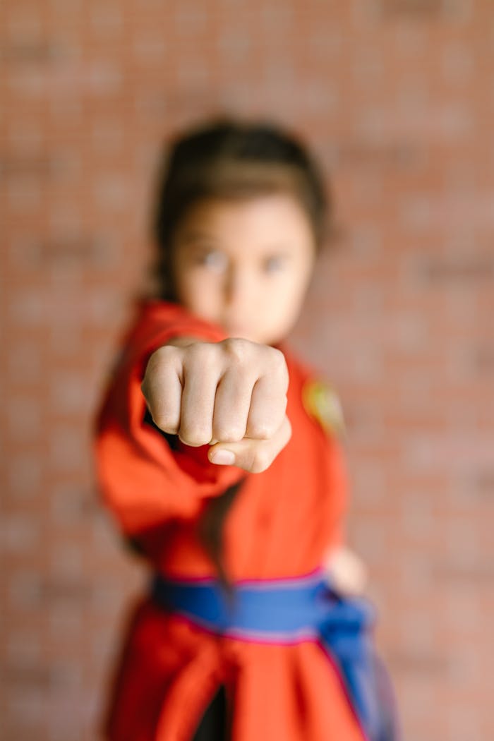 who-we-are Child in martial arts uniform performs a focused punch indoors.